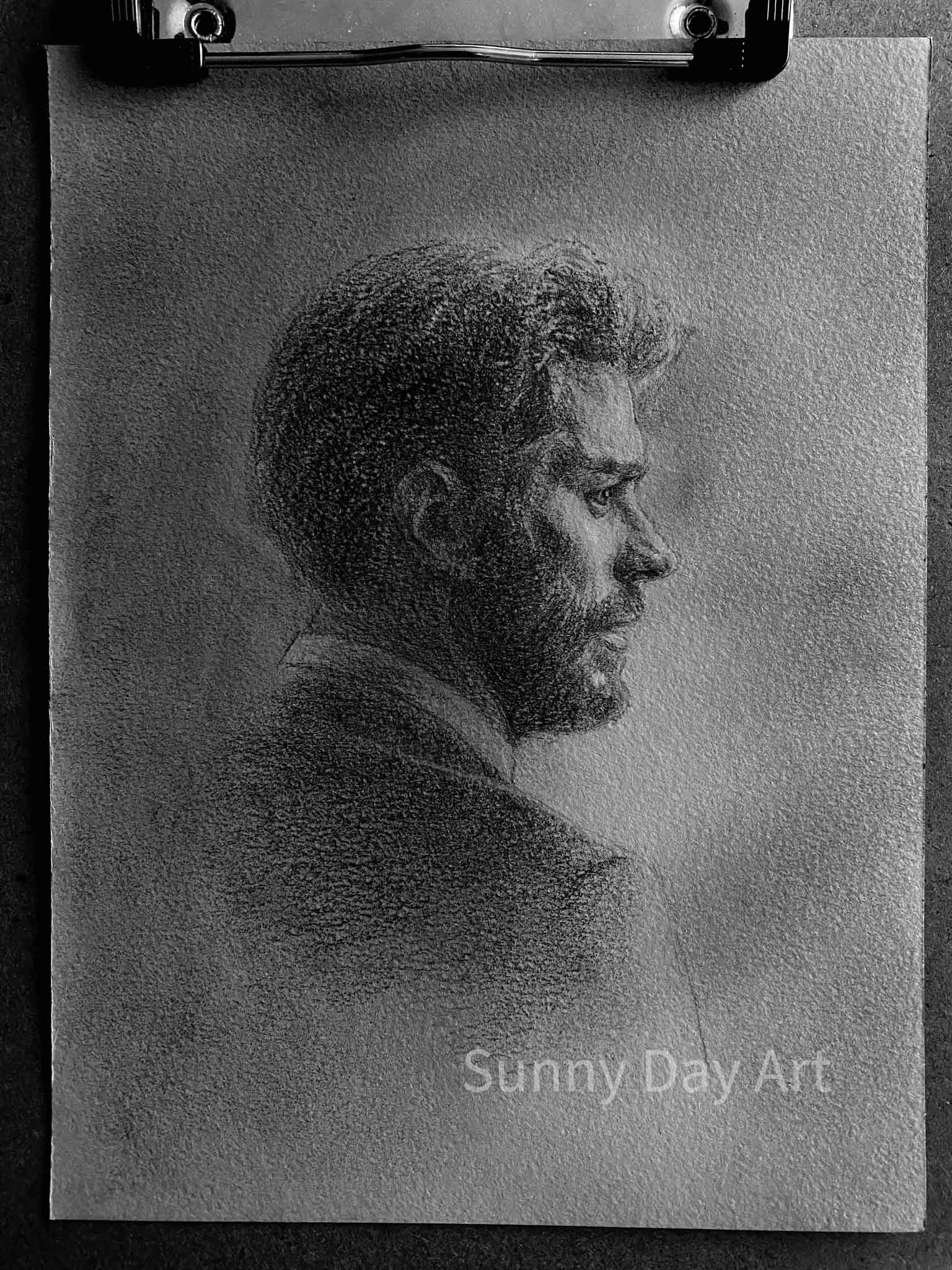 Portrait of a bearded man with neat hair, focused expression, on gray paper.