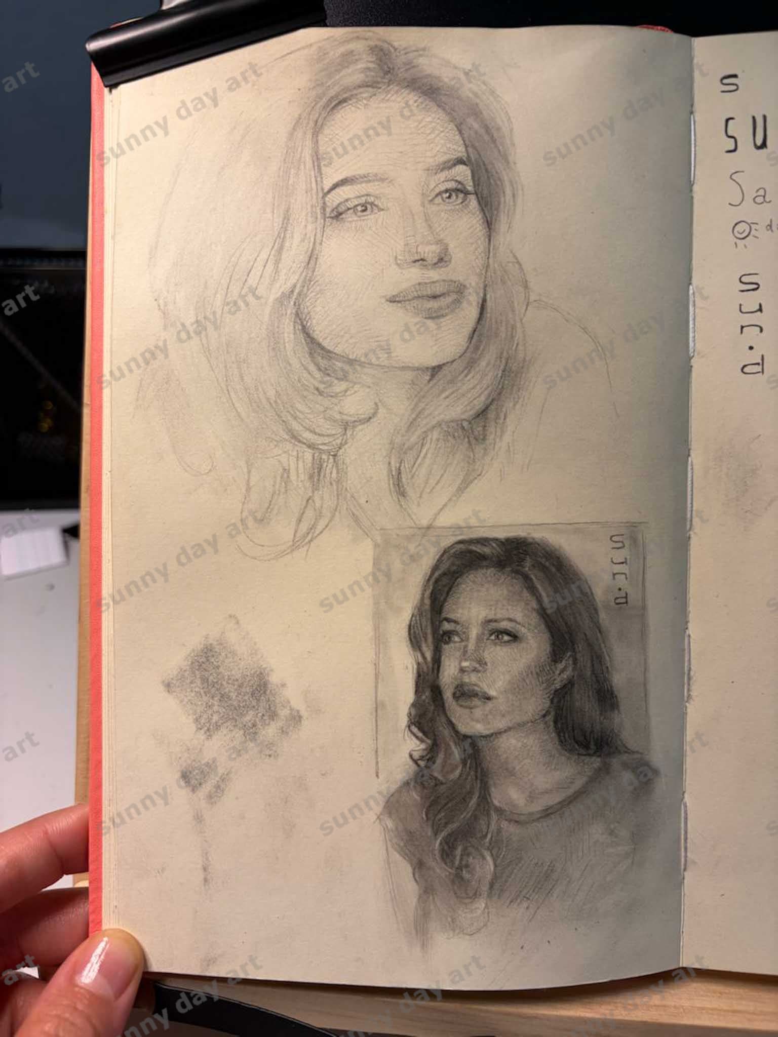 A sketchbook page featuring two sketches of Angelina Jolie—one graphite and one charcoal and graphite—viewed straight on.